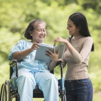 Happy Woman in a wheelchair reading a book with her daughter at the park